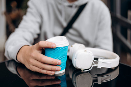 Paper cup and headphones on a cafe table with a teenage boy.の写真素材