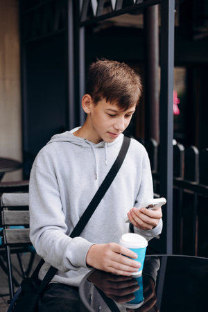 Teen boy using smartphone drinking from paper cup outdoors at cafe.の写真素材