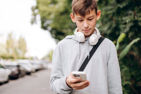 Teen boy walking on city street with headphones and smartphone.の写真素材