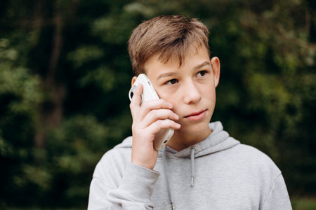 Portrait of serious teen boy talking on phone outdoors remote communication.の写真素材