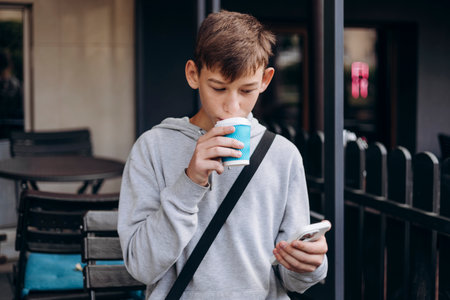Teen boy using smartphone drinking from paper cup outdoors.の写真素材