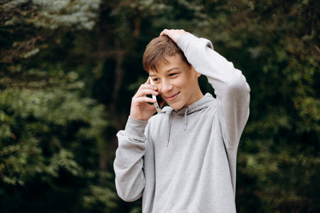 Portrait of teen boy smiling talking on phone outdoors holding his head.の写真素材