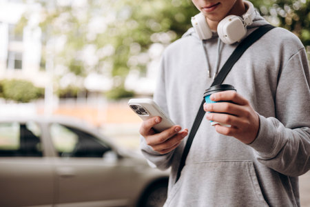 Teen boy using smartphone outdoors holding coffee cup, copy space.の写真素材