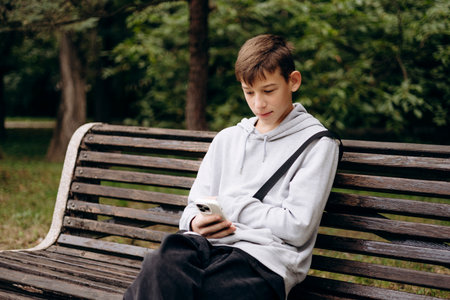 Teenage boy sitting on a park bench outdoors, looking at his smartphone.の写真素材