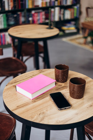 Pink book, smartphone and cups on table in bookstore cafe.の写真素材