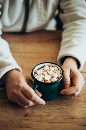 A man drinks cocoa with marshmallows at home at the kitchen table.の写真素材