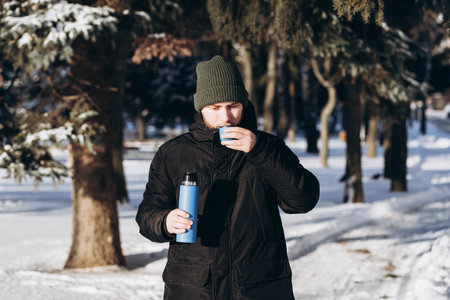 A young bearded man with a thermos enjoys a hot drink in the winter forest.の写真素材