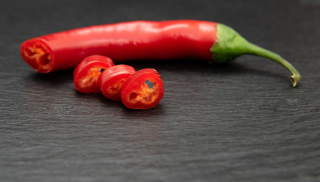 Red hot chili peper cut into slices. On dark plate backgroundの写真素材
