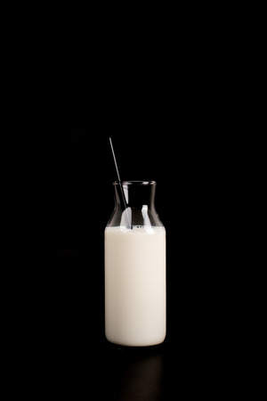 Fashionable bottle of milk on a total black background. Black straw in the bottle. The concept of a minimalist breakfast. Isolated on blackの写真素材