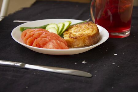 toast fried in a beaten egg lies on a white plate with chopped tomatoes, cucumbers and green onions....