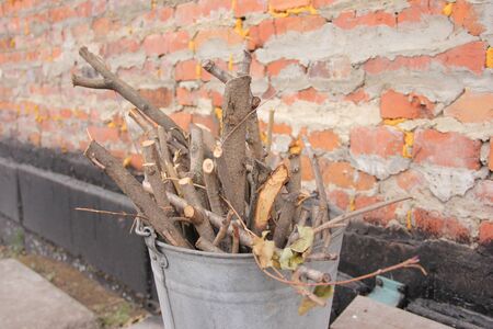 brushwood in a bucket for a stove or fireplace near a brick wall. Old firewood basket on a rustic wooden floor.の写真素材