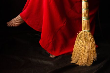 girl in a long red dress is sitting. beside the feet is a broom.の写真素材