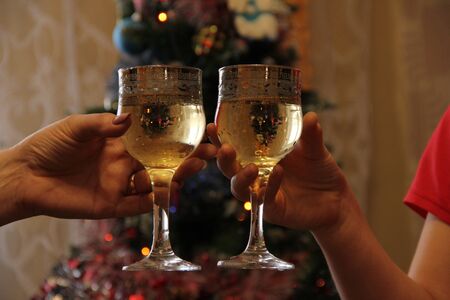 hands hold glasses of champagne against the background of the Christmas tree. Celebrating an...