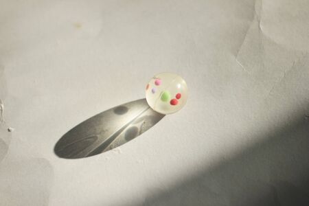 Transparent ball with colored balls inside casts a shadow on gray paper .
