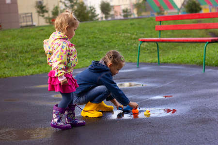 Beautiful girl in denim suit and yellow rubber boots plays with plastic duck and whale in a puddleの写真素材