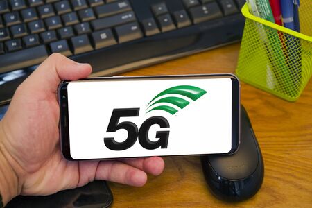 PIATRA NEAMT, ROMANIA - JULY 30, 2018: Hand holds a Samsung S8+ with 5G new radio logo on the screen, office background.のeditorial素材