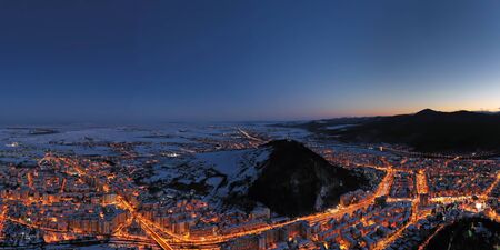 Drone view of night city lights and the mountains behind, Aerial landscape of Piatra Neamt in Romania, winter scene.の写真素材