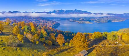 Autumn mountain panorama in Romanian Carpathians, mist cloud over the lake and colored trees, Bicaz...