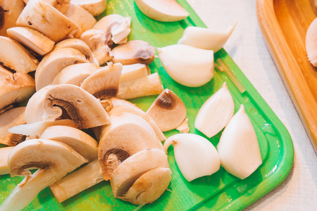 Sliced mushrooms champignons and garlic on a green tray. Fresh mushrooms and spices on the kitchen tray. Prepare for cookの写真素材