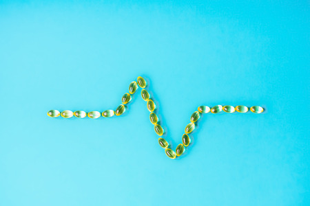 Yellow translucent tablets in the form of a line of a heart rhythm on a pastel blue background. Cardiogram of heart from pills on blue background. concept of medicines for cardiovascular system.の写真素材