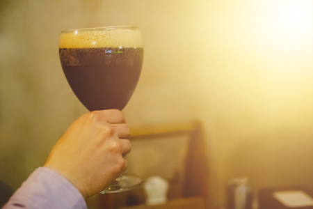Man in a shirt holds a mug of foamy Belgian beer in the club with copy space for textの写真素材
