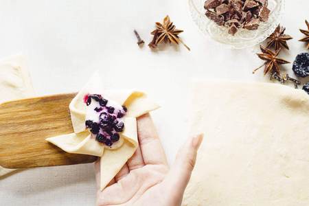 Cooking delicious sweets with jam and cinnamon and powder to tea. A woman's hand holds unfolded unpacked cake and wooden spatula. On white table lies sieve and scattered powder and cinnamon. Top viewの写真素材
