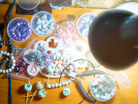 Accessories creating. Working disorder on the table. Buds of polymer clay, round pliers, working space.   Beautiful original beads from polymeric hand-worked clay.の写真素材