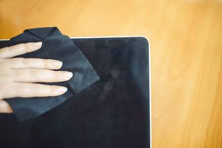 Close up female hand wipes a black rag black computer screen. Top viewの写真素材
