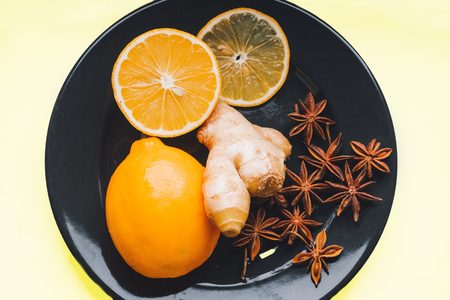 Chicory in a black plate with a whole lemon and two slices of lemon on a pastel yellow background