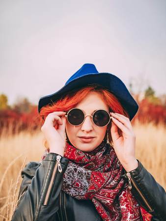 Portrait of a awesome woman in glasses, a blue hat, a leather jacket in a park in autumnの写真素材