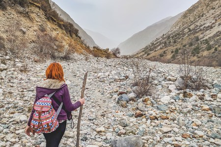 Hiker woman with backpack. Traveler explorer young woman standing on rocky stone and looking at mountain valley in summer, rear view.の写真素材