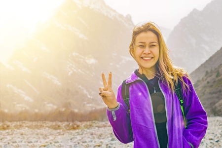 A woman in the mountains shows a sign of peace. Female travel in mountains alone. Spring weather, calm scene.の写真素材