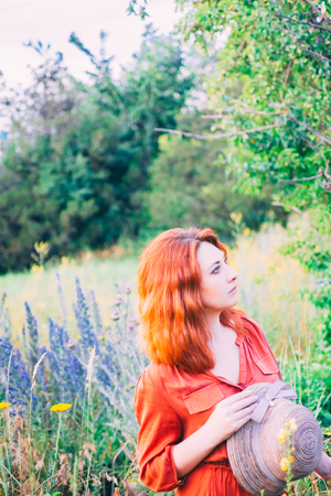 Girl on dandelion on green field. A lonely beautiful girl in a red dress is walking and enjoying the greenery and dandelion.の写真素材