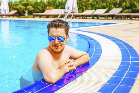 Man looks out of the pool, hanging on the railing. Young man having a good time in the swimming pool.の写真素材