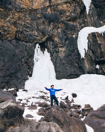 Belogorka, Kyrgyzstan - March 25, 2018: Guy in a blue jacket in the mountains and icy waterfallのeditorial素材