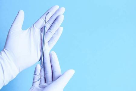 Surgical tool in a doctor's hand in a glove on a blue backgroundの写真素材