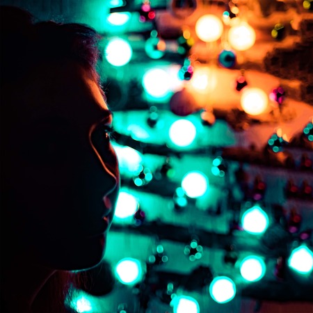 A woman on a Christmas night against a background of a bright Christmas tree made of twigs hanging on the wall and decorated with a garland and toys in the dark.の写真素材