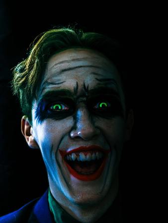 Young man celebrates halloween. Dark creepy white face, green eyes and hairs, laughing in the dark. Halloween in October.の写真素材