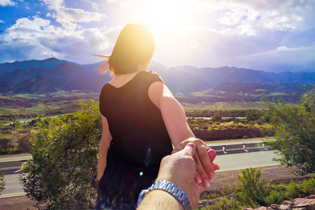 Guy follows his girlfriend holding her hand on pedestrian travel outdoors in mountains.の写真素材