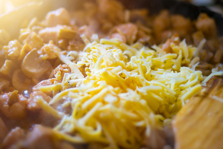 Grated cheese on chicken with mushrooms in sour cream sauce in a frying pan with a wooden spoon.の写真素材