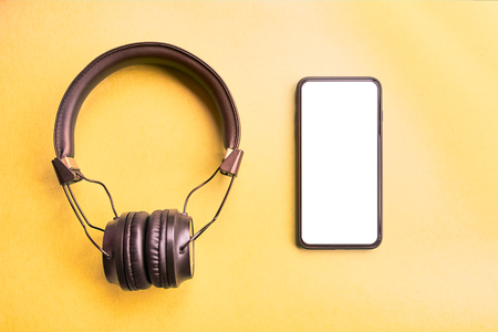 Black wireless headphones for music sound Isolated and black frameless smartphone on colorful yellow background, top view. Mock-up, design elementsの写真素材
