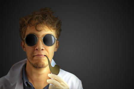 Amazing crazy professor with a smoking pipe in a white robe and dark sunglasses on a black wall background. Halloween costume with copy space for text.の写真素材