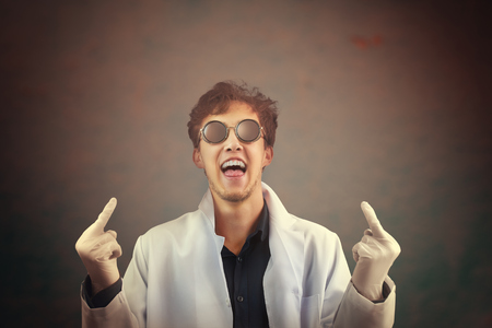 Crazy laughing man doctor in white coat and sunglasses giving you fingers in the center. Flipping off the middle finger bird gesture on dark background. The hands is selectively in focus. Halloweenの写真素材