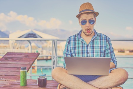 Man on vacation, sits on the pier and works. Guy shocked on something on laptopの写真素材