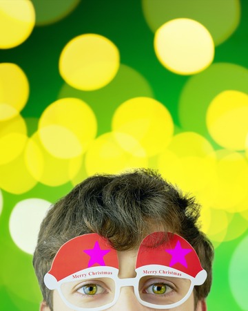 Portrait of cheerful man in Christmas glasses. , attractive man on green sparkles background with copy space for text, look over glasses. Vertical crop 4x5の写真素材