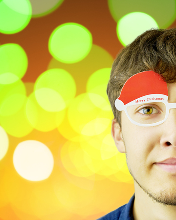 Portrait photo of smiling nerdy guy with christmas glasses on a christmas yellow sparkles orange background. Copy space for text.の写真素材