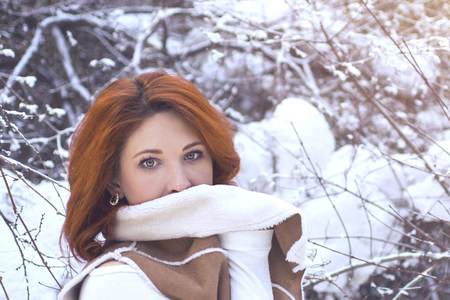Beautiful girl with long curly hair in white knitted vest having fun outdoor in winter forest under snowflakes. Pretty young model standing on white background and looking at camera.の写真素材