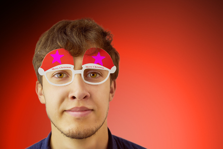 Portrait photo of smiling nerdy guy with christmas glasses on red background. Copy space for text.の写真素材