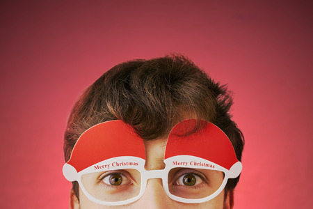 Young man with glasses with text merry Christmas on a bright red background. Holiday costumeの写真素材