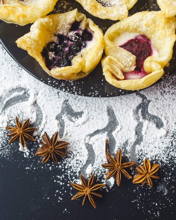 Homemade cookies with jam, on a black desk. black background. Cooked at home buns are waiting for their tea. View from above. Biscuits with jam and scattered powder and cinnamon on a black table.の写真素材